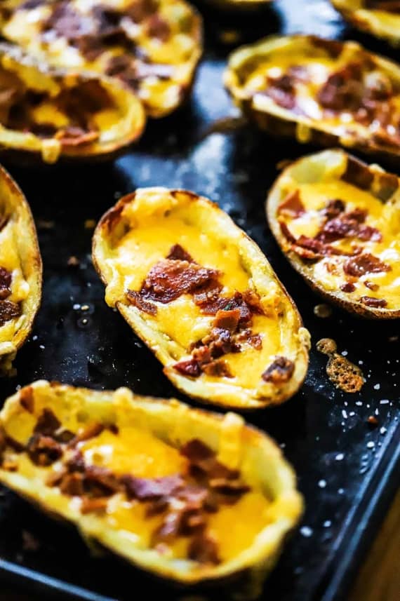 A black baking sheet filled with loaded potato skins.