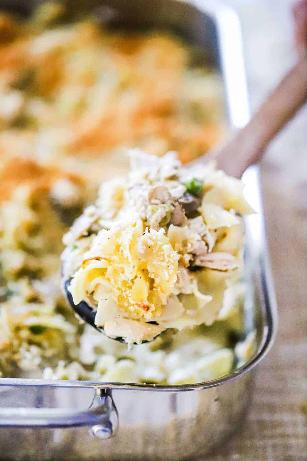 A large wooden spoon filled with turkey tetrazzini over a pan filled with the same. 