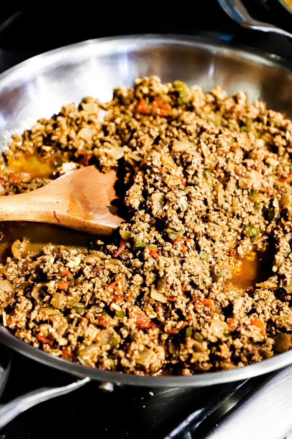 A large silver skillet filled with prepared taco meat with a wooden spoon in the middle of it. 