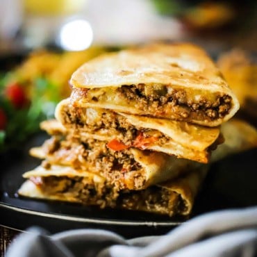 A row of taco quesadillas leaning against each other on a black serving plate.