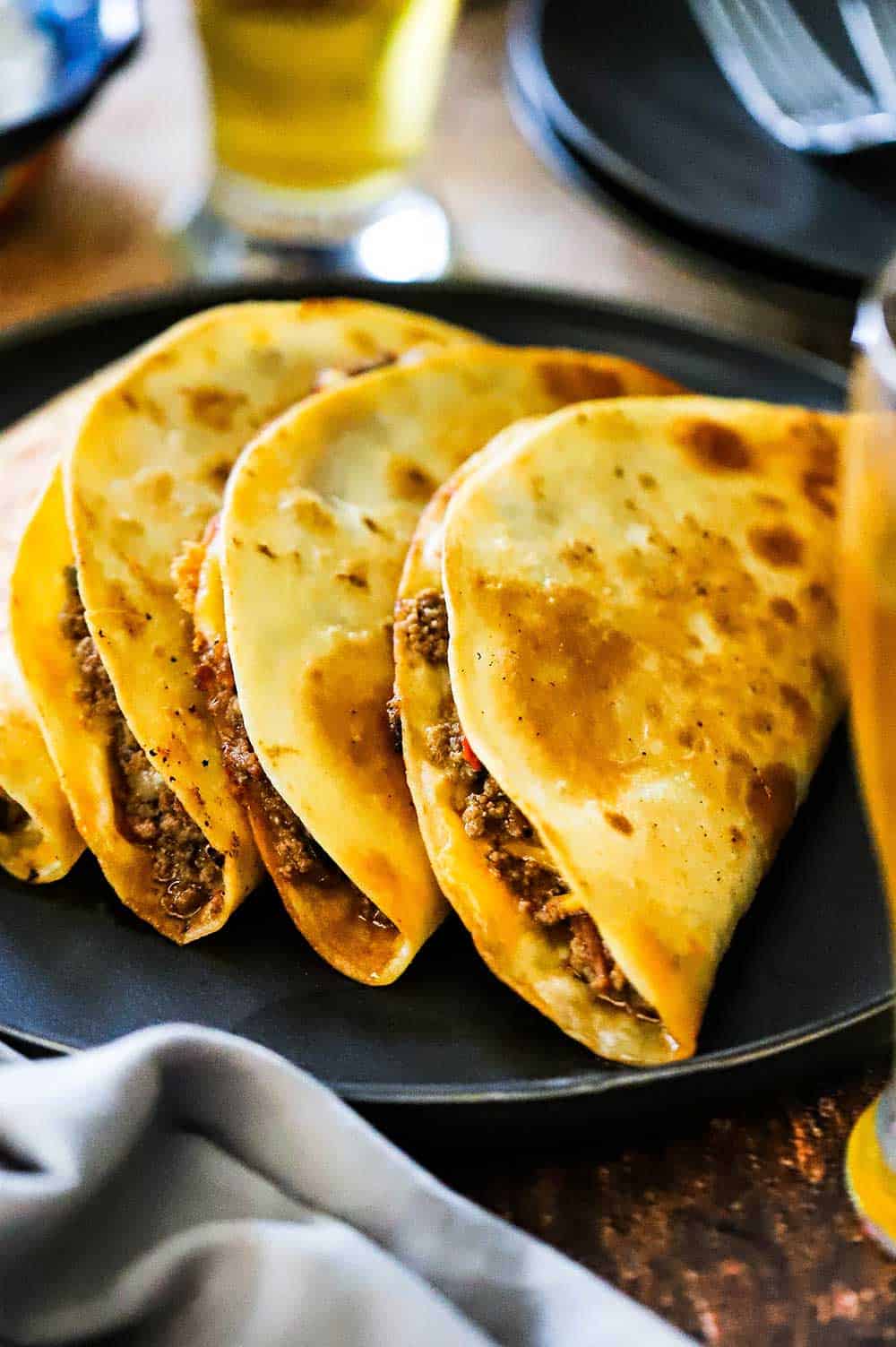 A row of taco quesadillas leaning against each other on a black serving plate. 