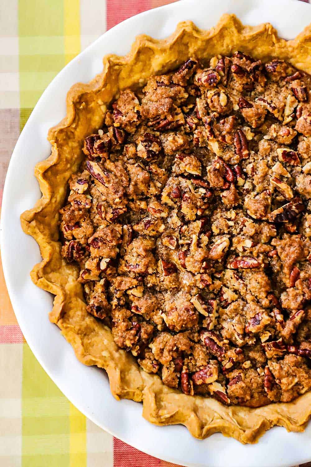 A sweet potato pie in a pie crust with fluted edges sitting in a white pie dish on an autumnal place setting. 