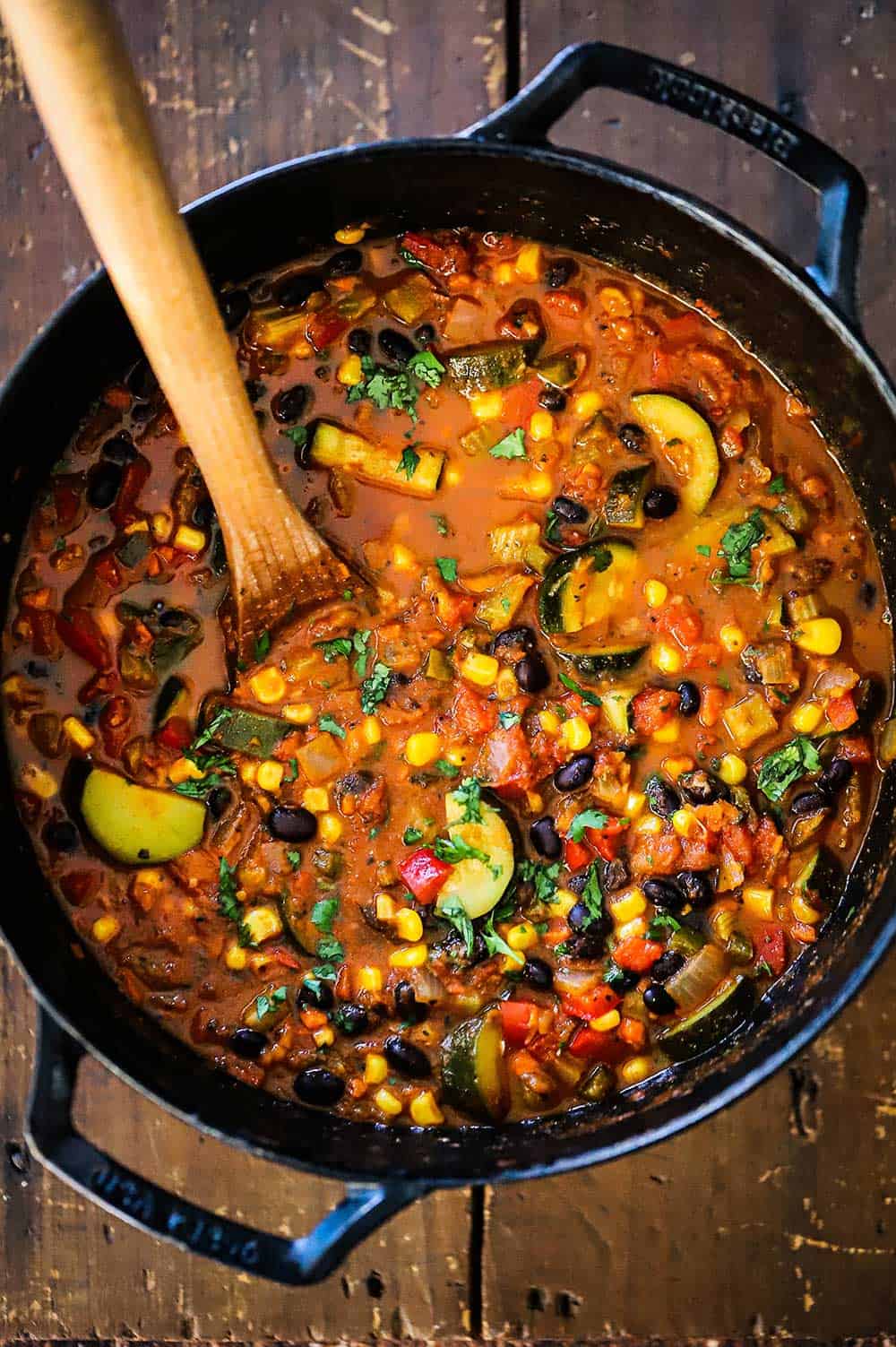 A large cast-iron pot filled with vegetable chili with black beans.