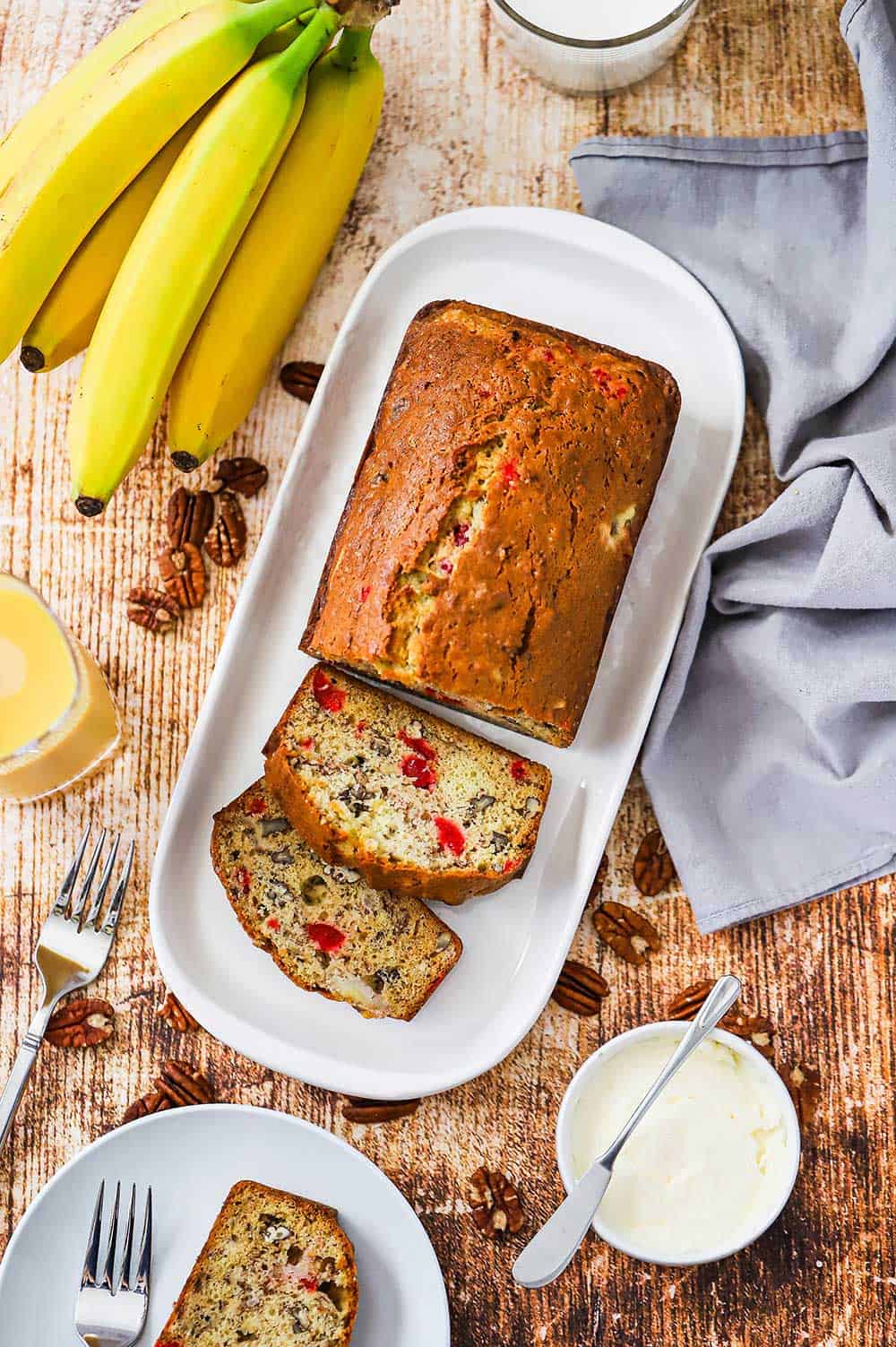 A loaf of banana nut bread with a couple slices that have been cut on a rectangular white serving dish.