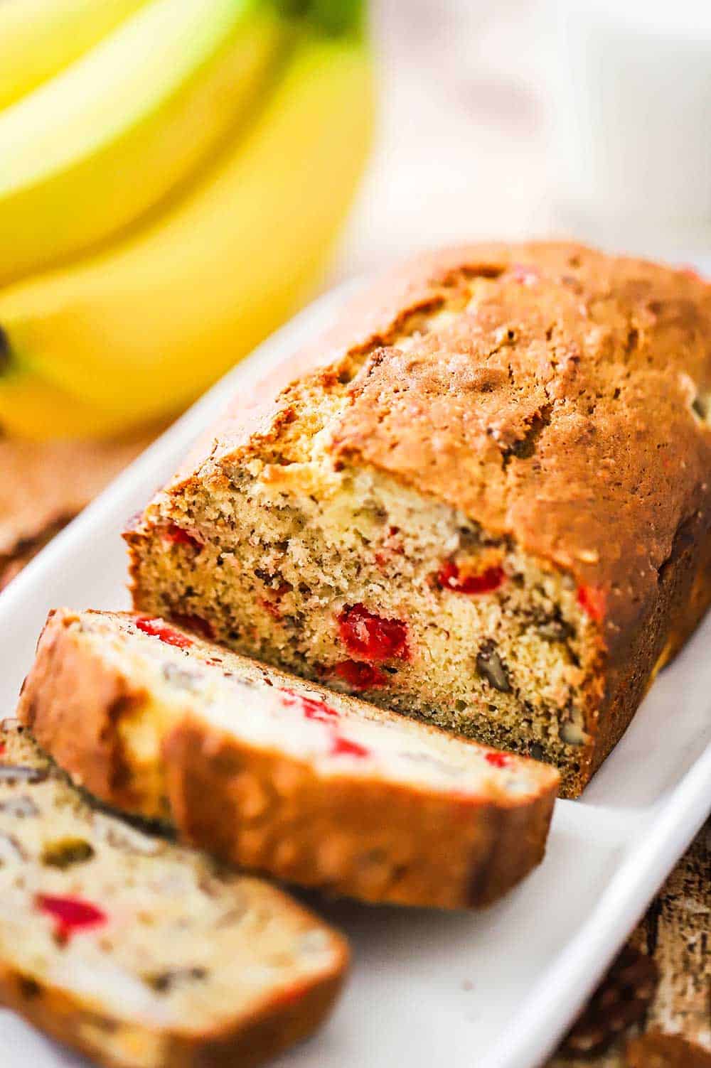 A loaf of banana nut bread with a couple of slices cut sitting on a white serving dish.