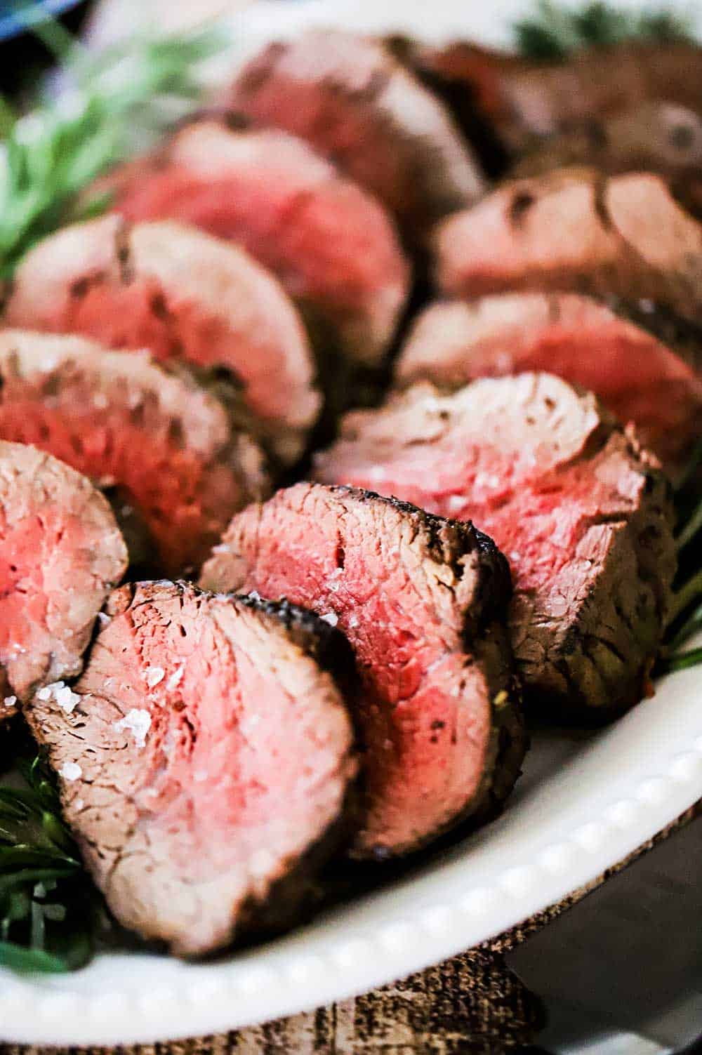 Two rows of sliced of beef tenderloin on a white serving platter. 