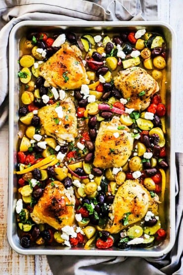 Sheet Pan Greek Chicken fully cooked with vegetables and feta cheese sprinkled all over the top.