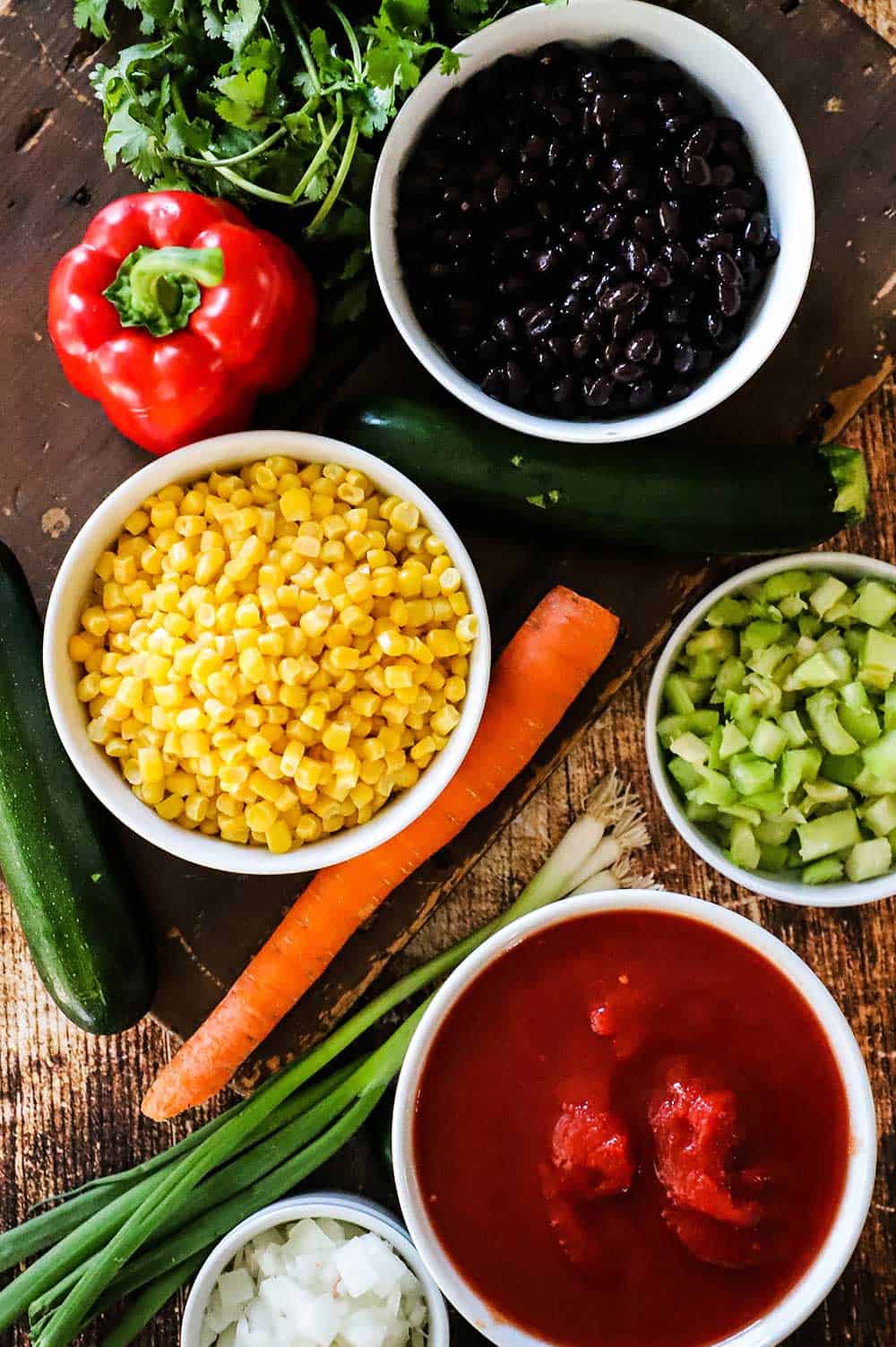 An assortment of bowls of fresh tomatoes, corn, celery, onions, and black beans.