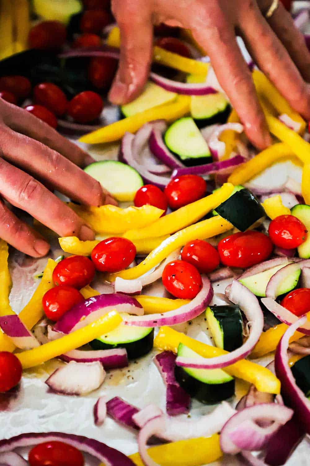 A pair of hands spreading out cut vegetables on a large sheet pan. 