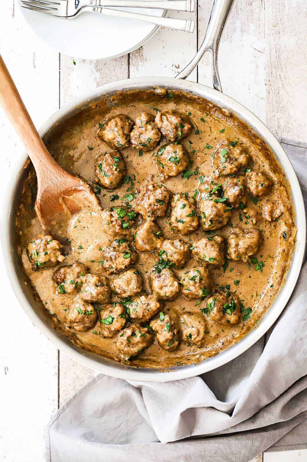 A large stainless steel skillet filled with Swedish meatballs and wooden spoon.