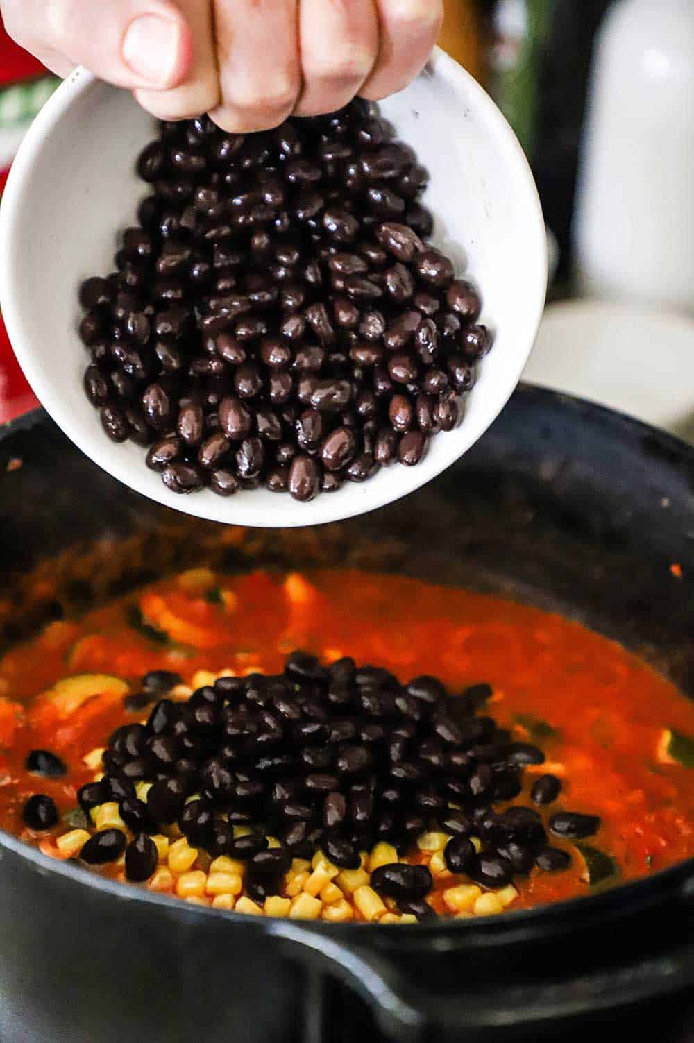 A person transferring black beans into a pot of chili.