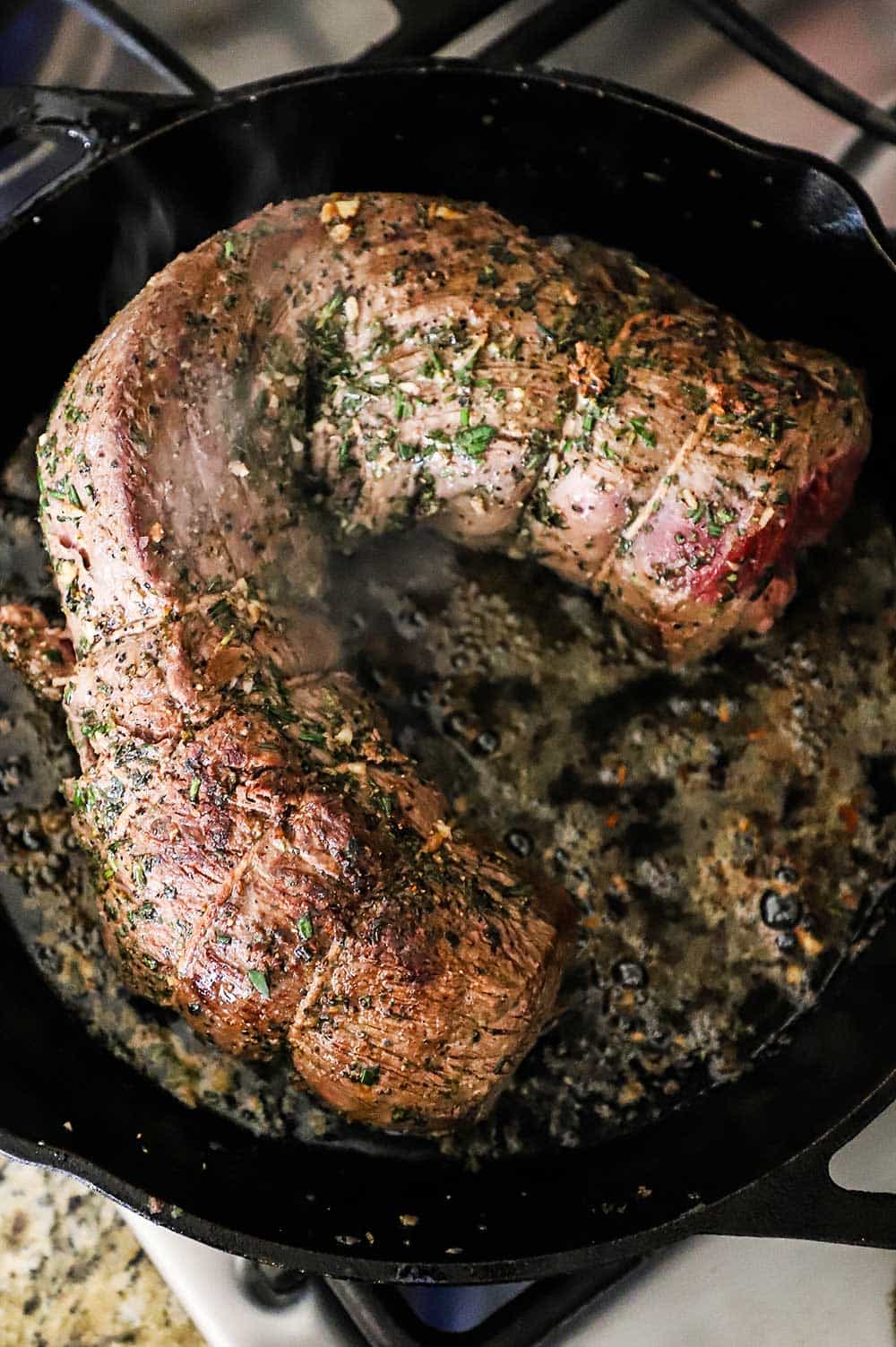 A large beef tenderloin roast that has been seared in a large black cast-iron skillet. 