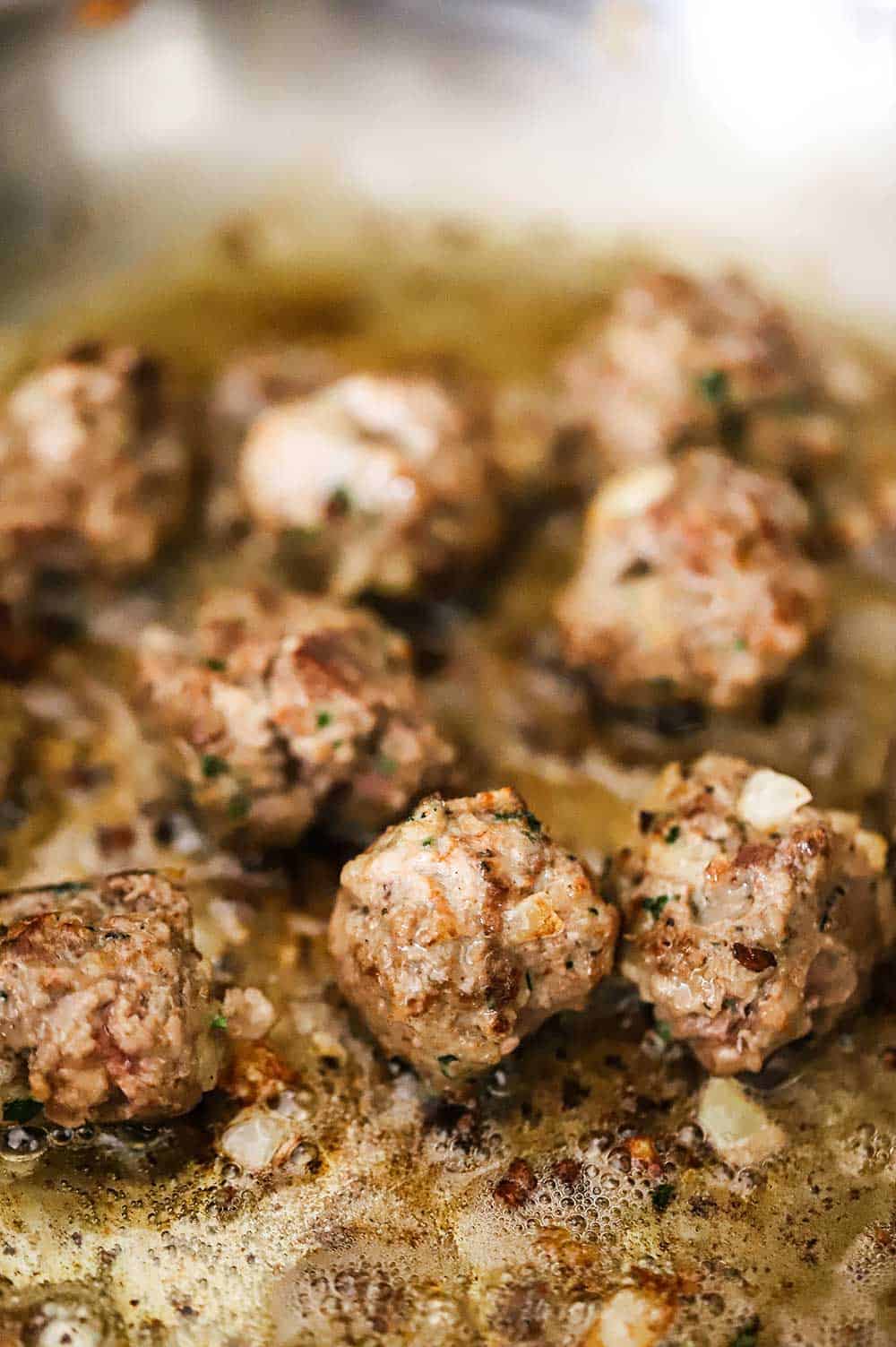 Swedish meatballs being seared in a large silver saucepan.