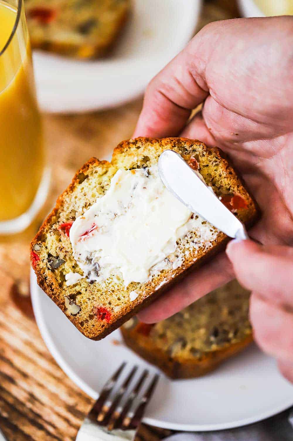 A person smearing softened butter onto a slice of banana nut bread. 