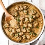 A large stainless steel skillet filled with Swedish meatballs and wooden spoon.