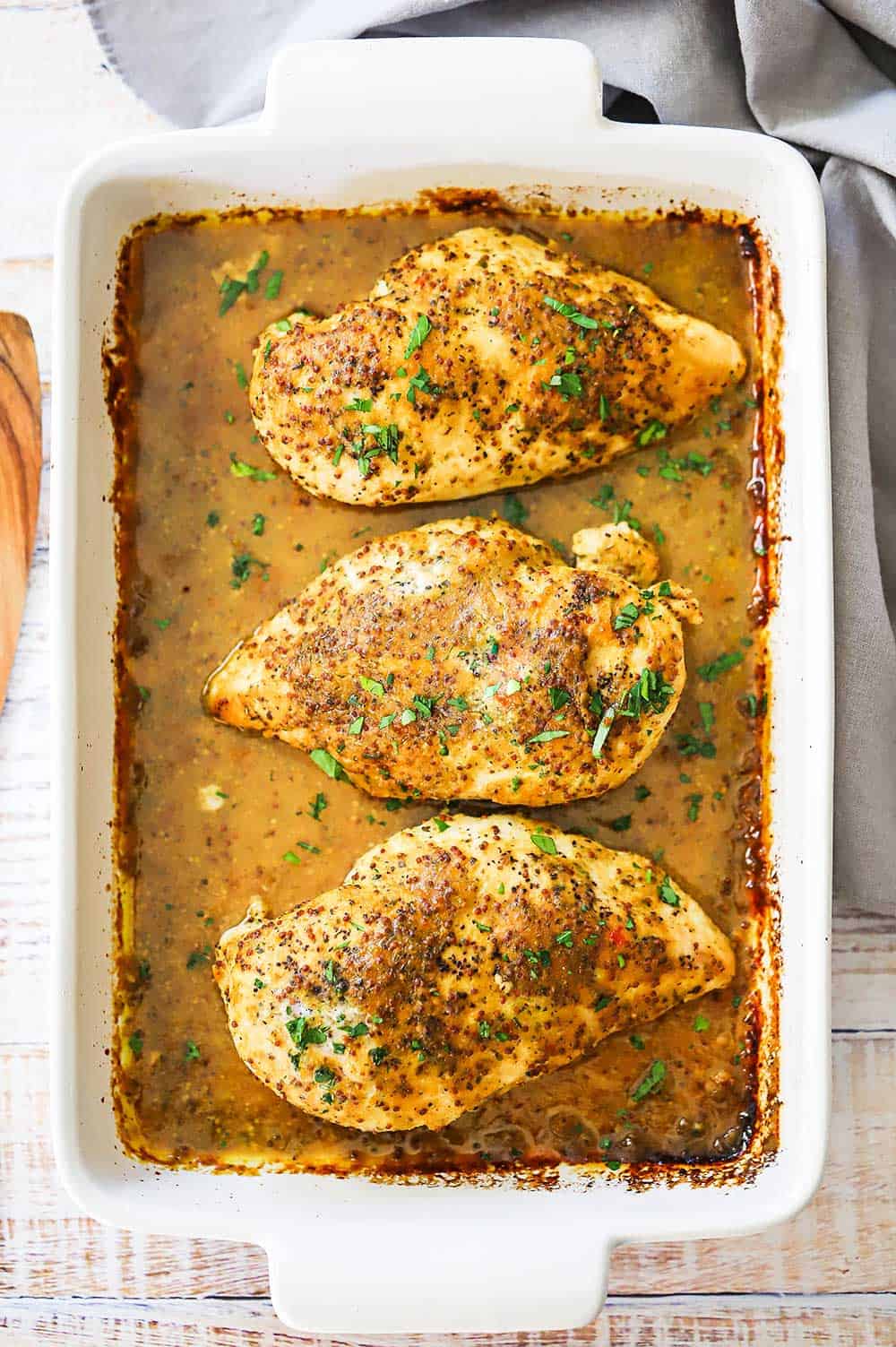 A white 9 by 13-inch baking dish filled with three whole boneless skinless chicken breasts baked with a honey mustard sauce on them.