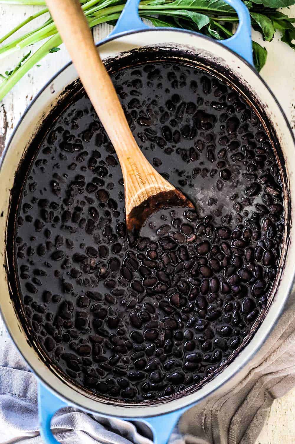 A large oval blue Dutch oven filled with Mexican black beans with a wooden spoon in the middle.