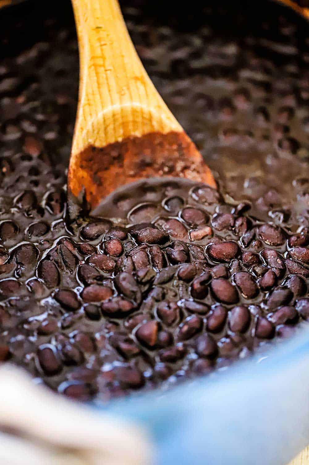 Mexican black beans in a pot being stirred with a wooden spoon.