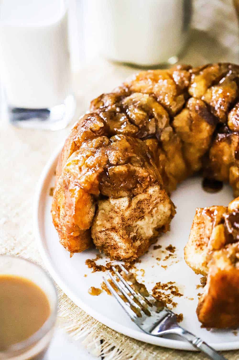 Homemade monkey bread with a few pieces missing on a white round platter next to a glass cup of coffee. wi