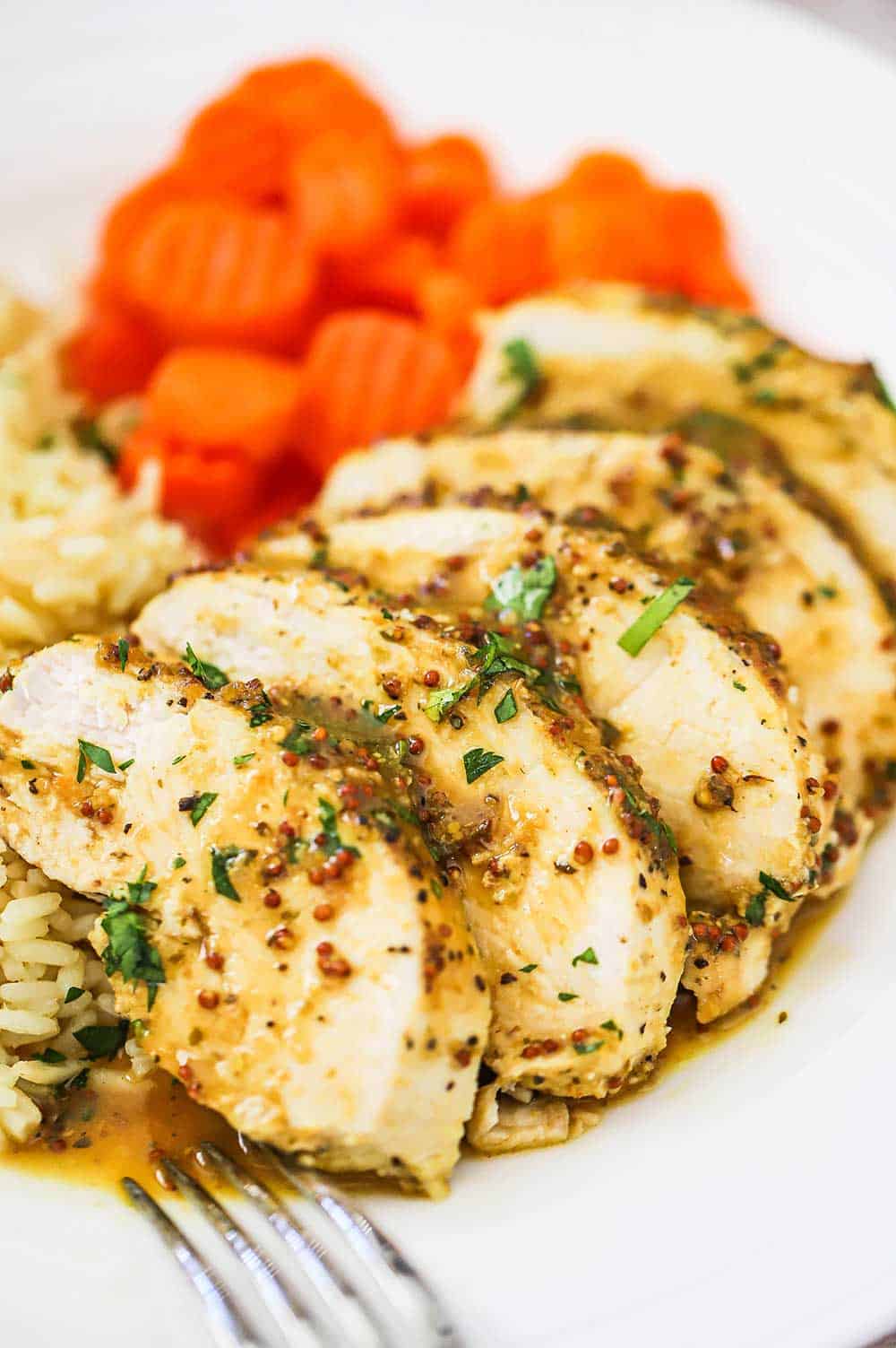 A white dinner plate filled with 5 slices of cut baked honey mustard chicken sitting next to sliced carrots and rice pilaf also on the plate.