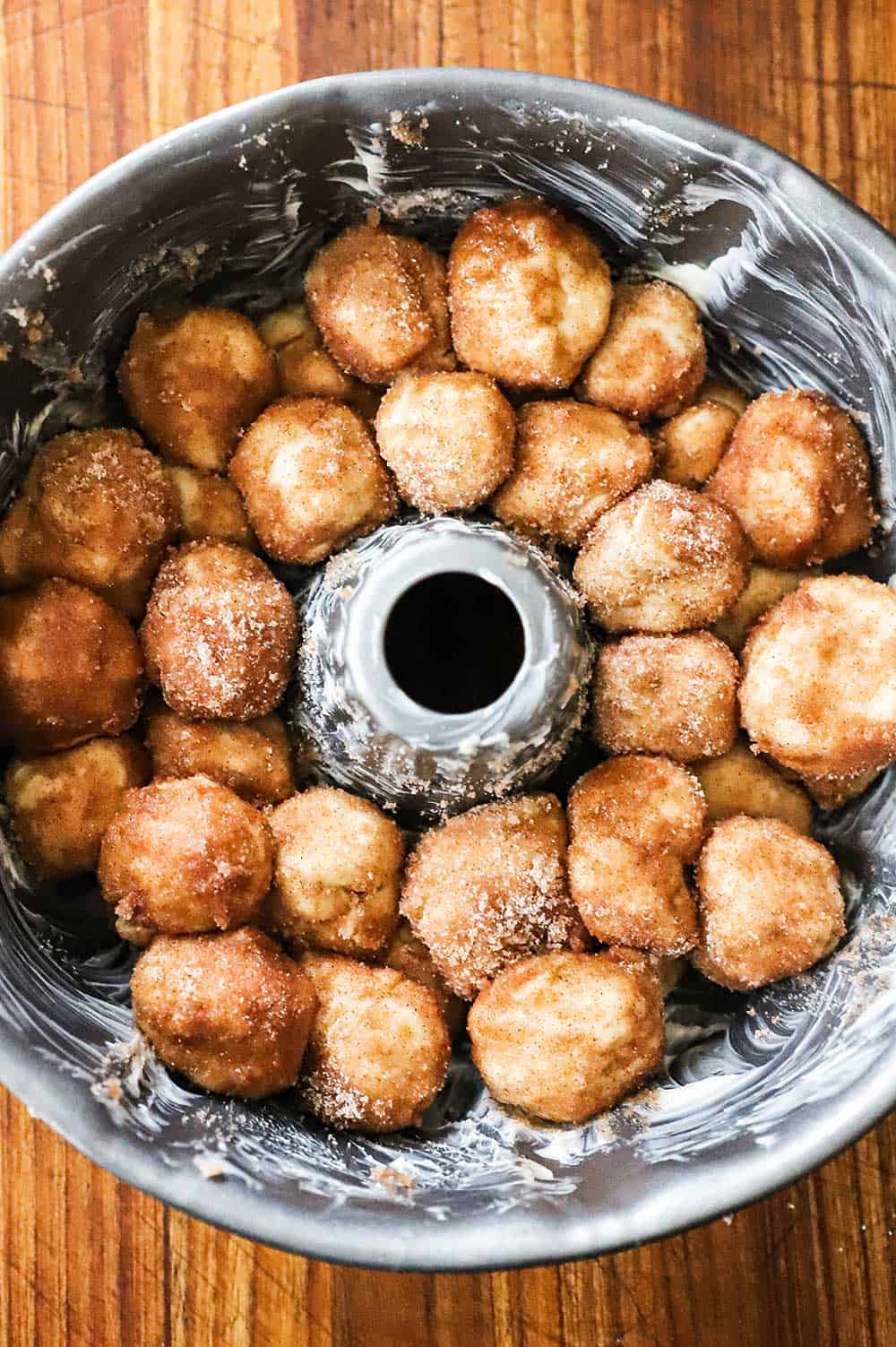 Uncooked balls of dough that are coated in butter and cinnamon sugar sitting in a greased bundt pan.