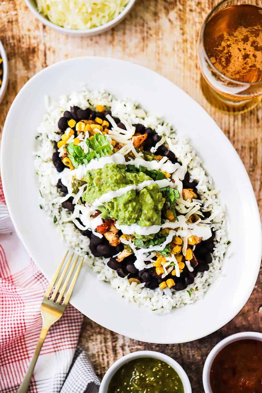 A chicken burrito bowl pile high in a white oval dish with a gold fork next to it.