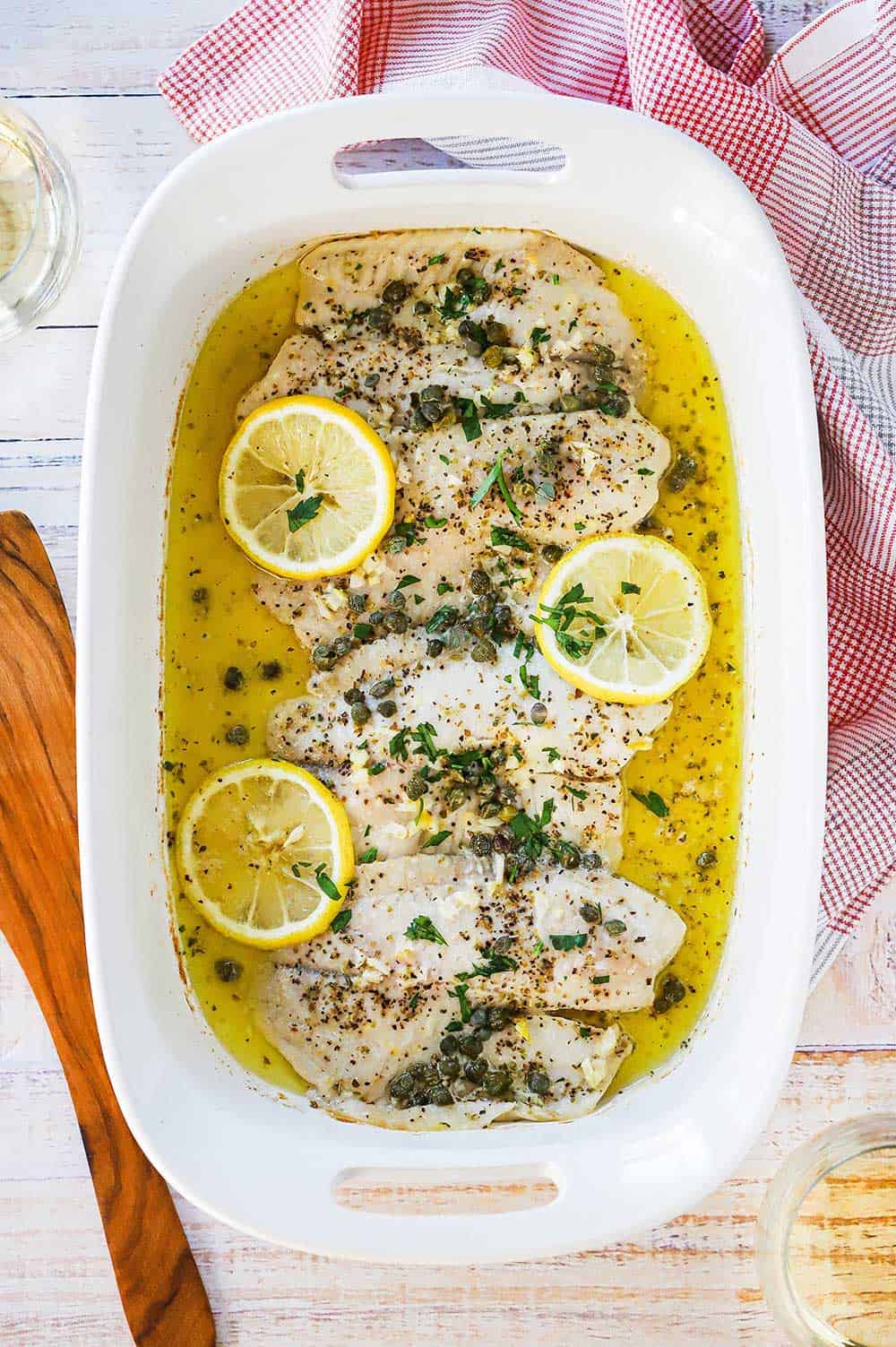 A white 9 by 13 baking dish filled with baked tilapia with lemon garlic sauce. 