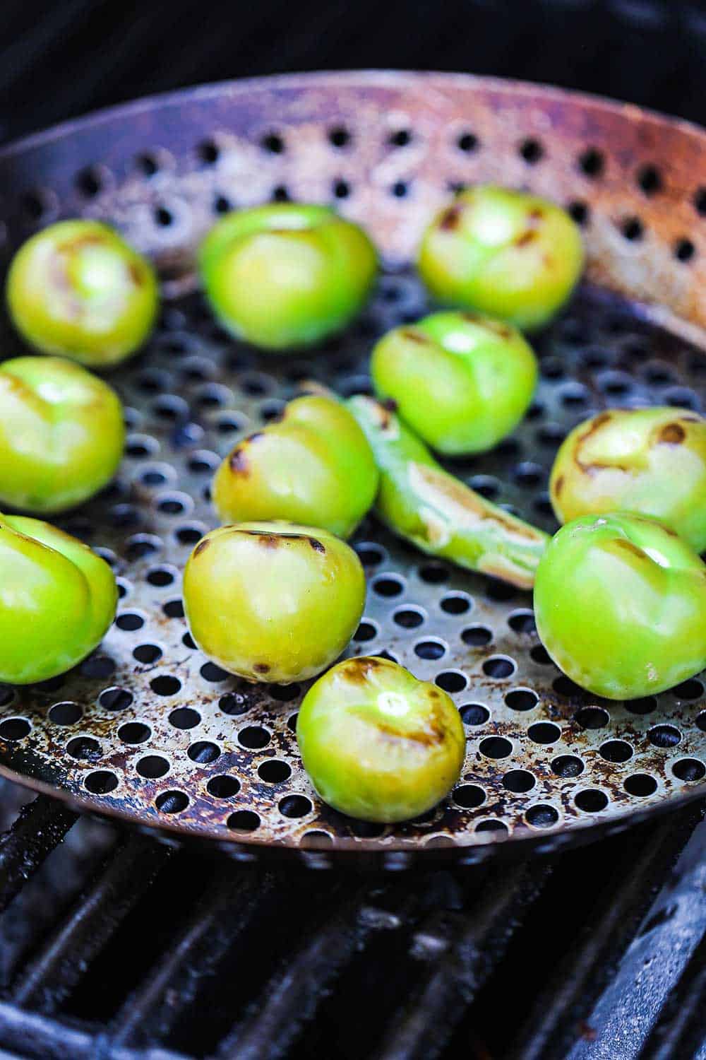 A circular grill pan filled with tomatillos and a serrano pepper that have been roasted and lightly charred.