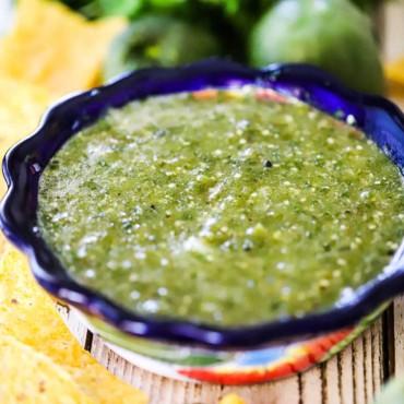 A festive bowl filled with salsa verde and surrounded by corn tortilla chips.
