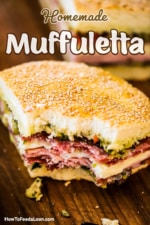 A quarter slice of a muffuletta sandwich with a bite taken out of it.