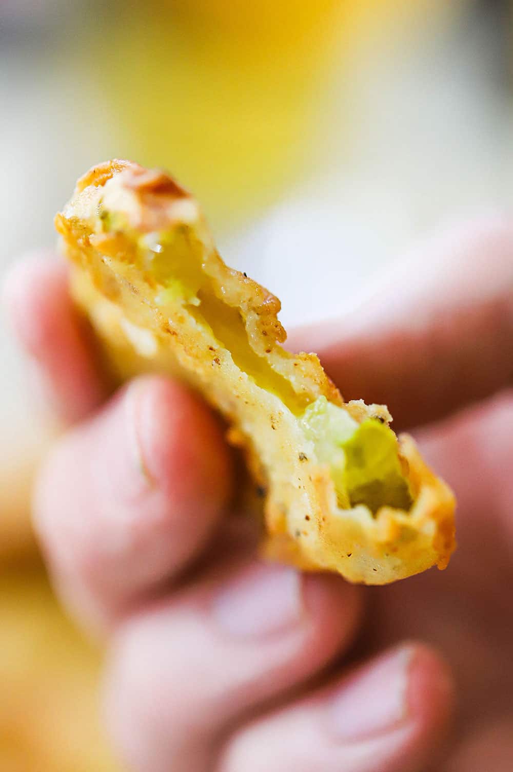 A hand holding up a fried pickle that has a bite taken out of it.