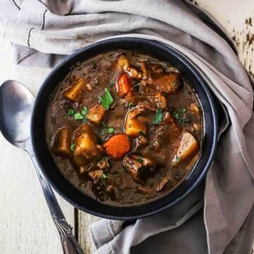 A blue soup bowl filled with slow-cooker beef stew and garnish with chopped fresh parsley.