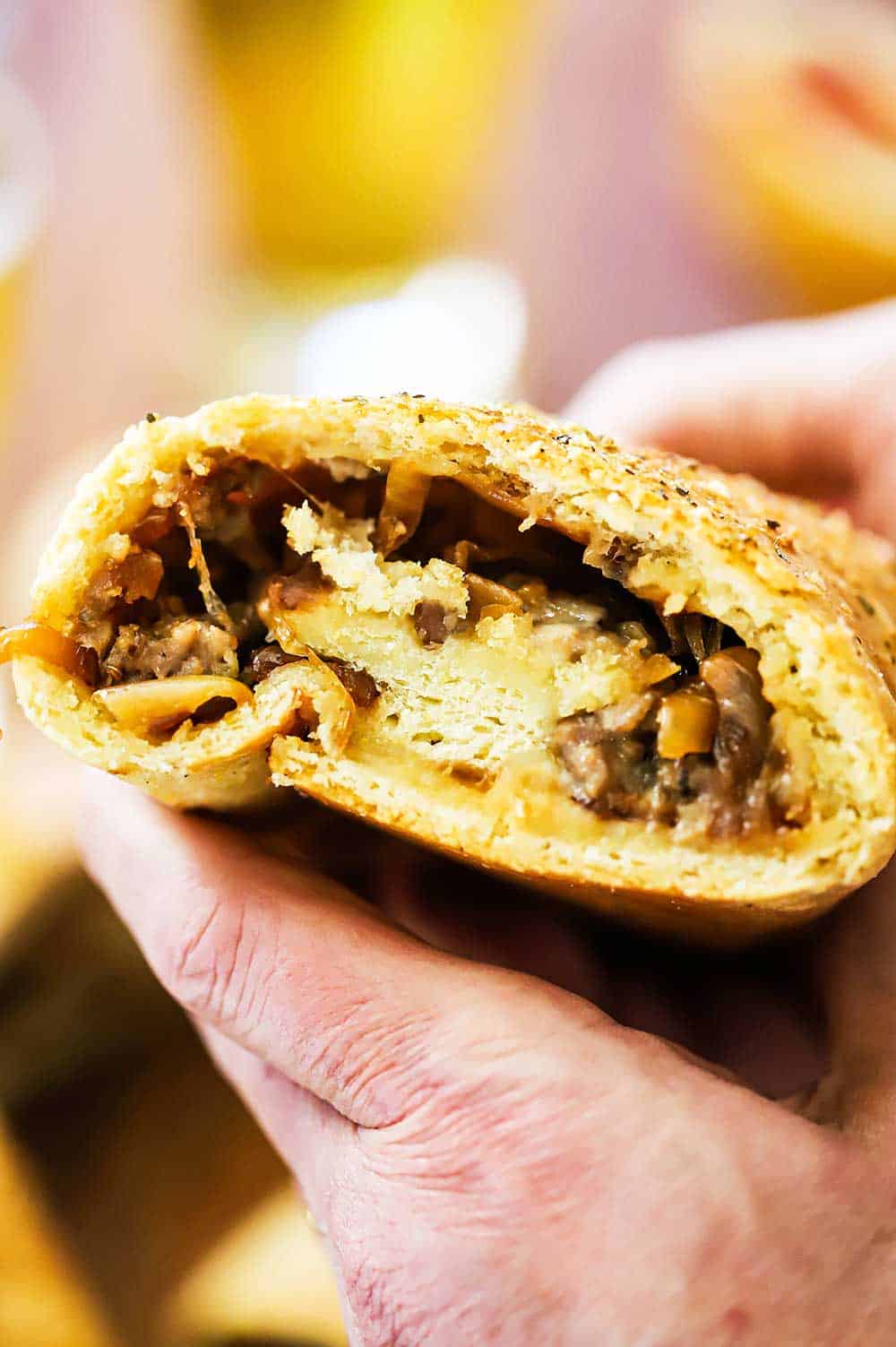 A pair of hands holding up sausage bread that has been cut in half revealing the sausage and caramelized onions.