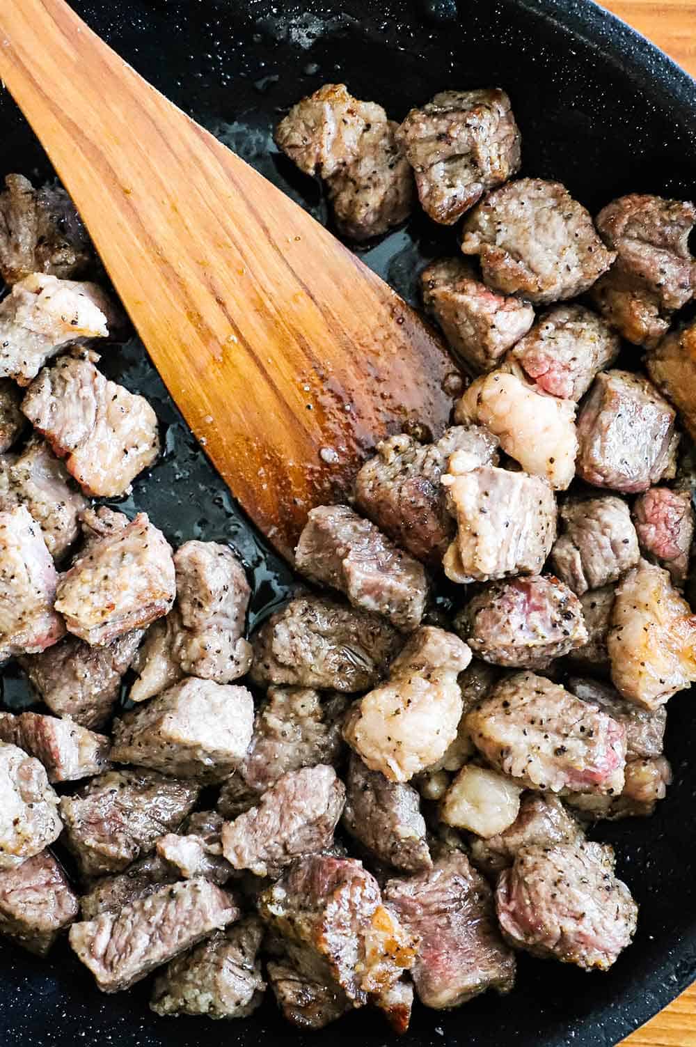 A large black skillet filled with pieces of beef that has been seared.