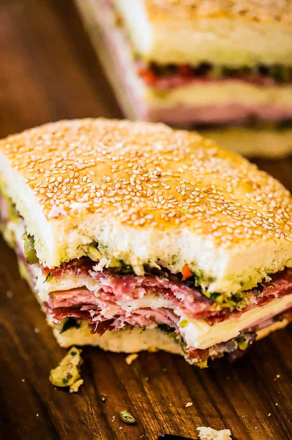 A quarter slice of a muffuletta sandwich with a bite taken out of it.