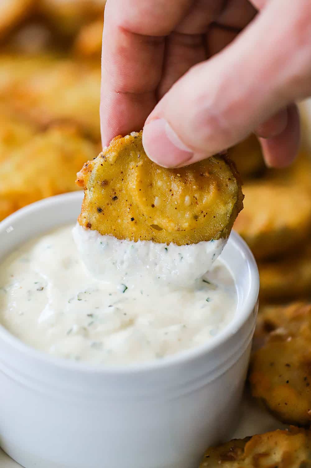 A person dipping a fried pickle into a small bowl filled with Ranch dressing.