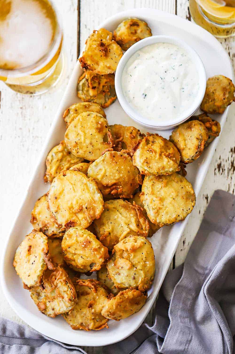 A oval white platter filled with fried pickles nestled next to a small white bowl filled with Ranch dressing.