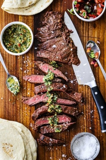 An overhead view of carne asada that has been sliced and topped with chimichurri sauce and finishing salt.