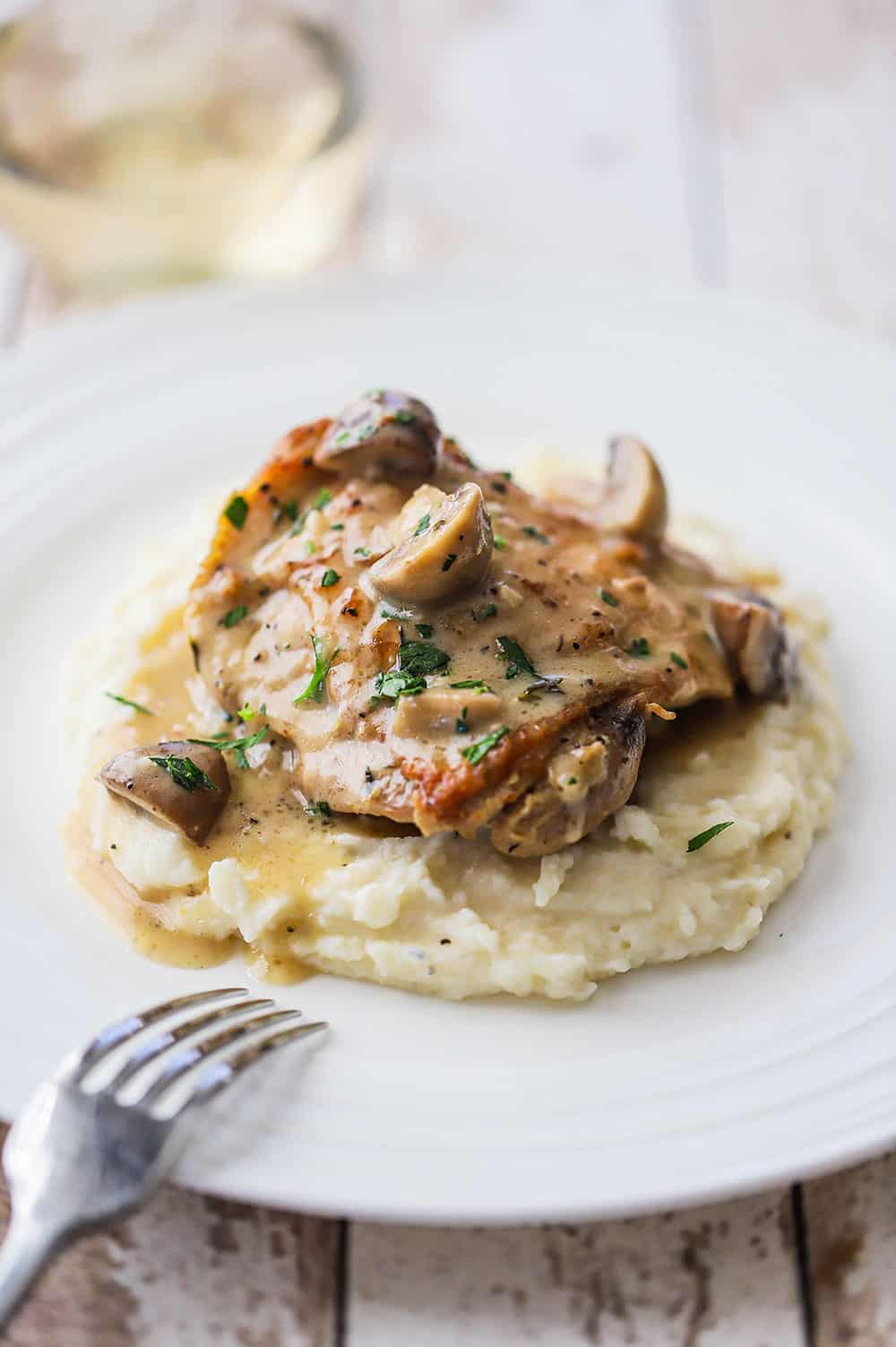 A plate of chicken fricassee with a seared chicken thigh sitting on a bed of mashed potatoes with a mushroom gravy poured over the top.
