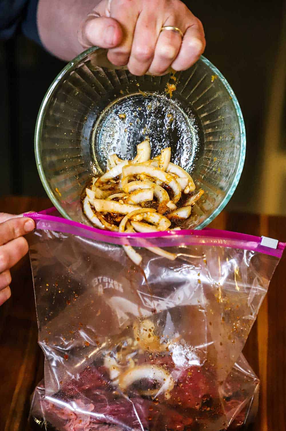 A marinade filled with sliced onions being poured into a plastic baggie filled with flap steak.