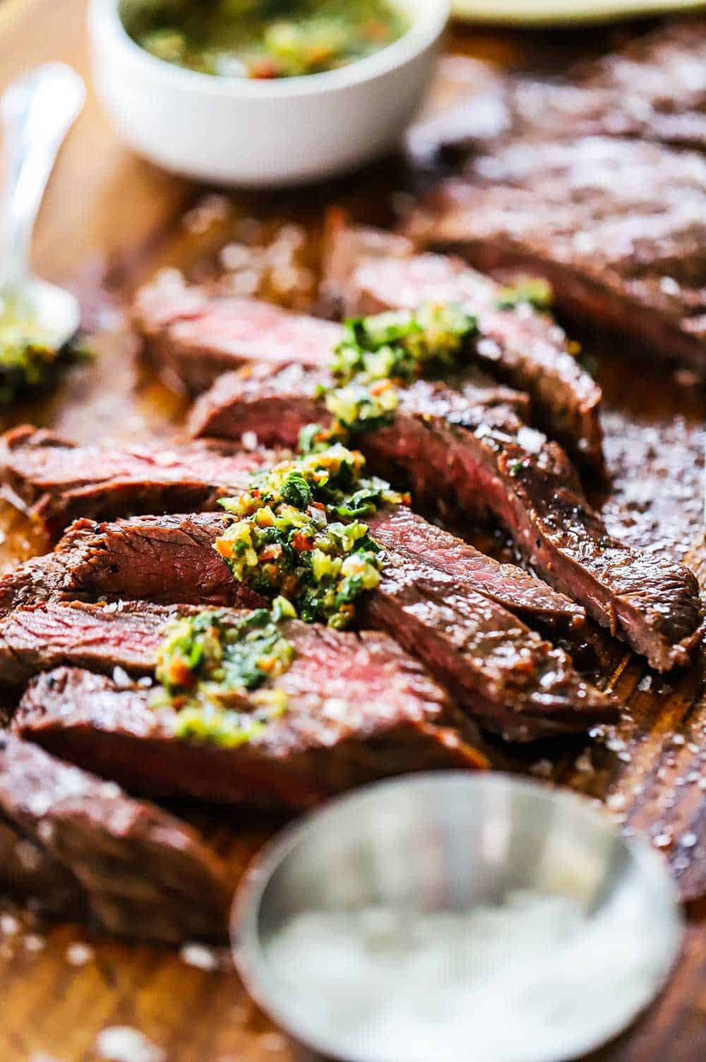 Carne asada on a cutting board that has been sliced and drizzled with chimichurri sauce.