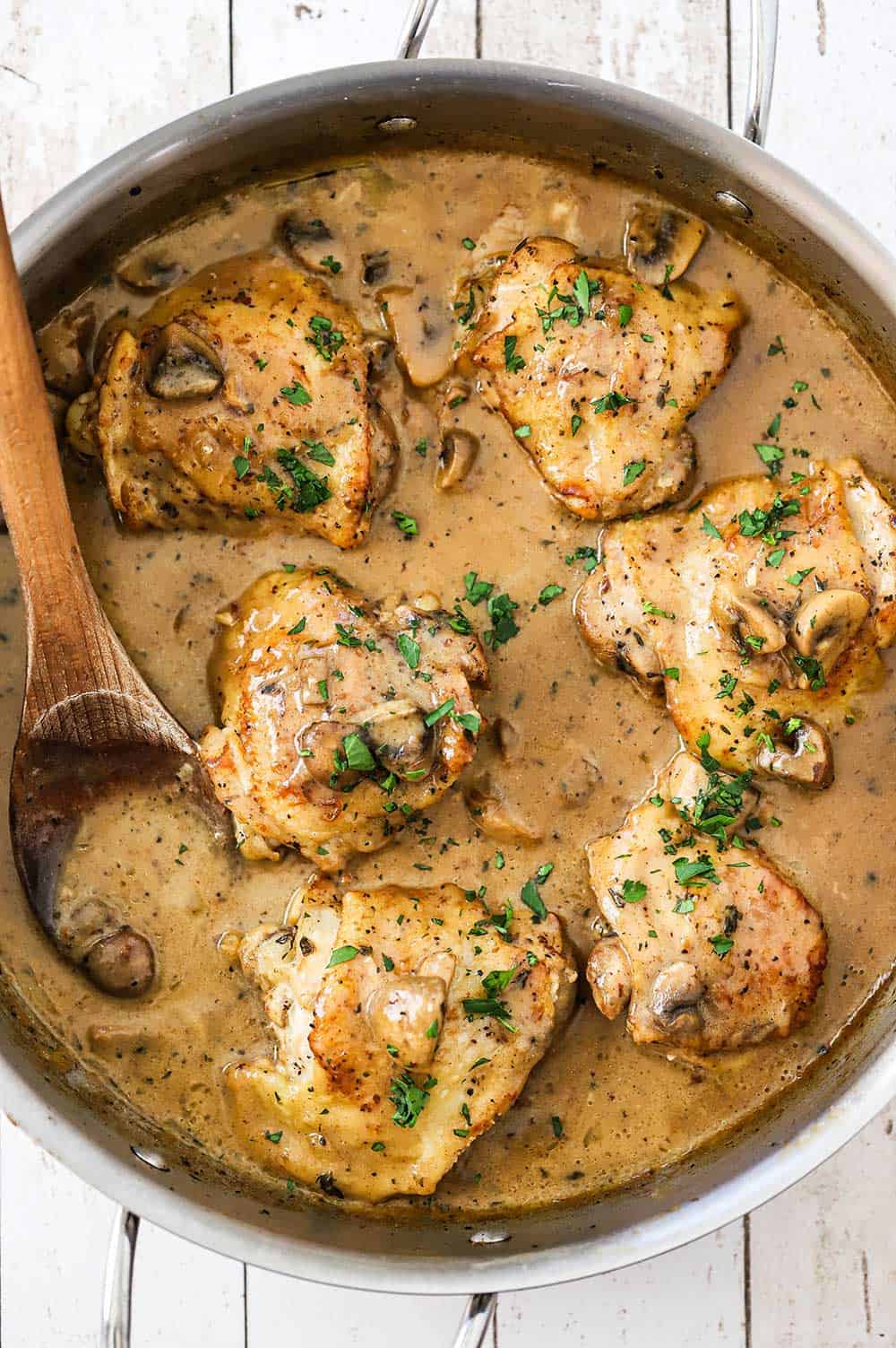 An overhead view of a stainless steel skillet filled with six pieces of chicken fricassee with a creamy mushroom sauce.