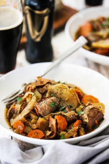 A white bowl filled with Dublin coddle next to a glass of stout beer.