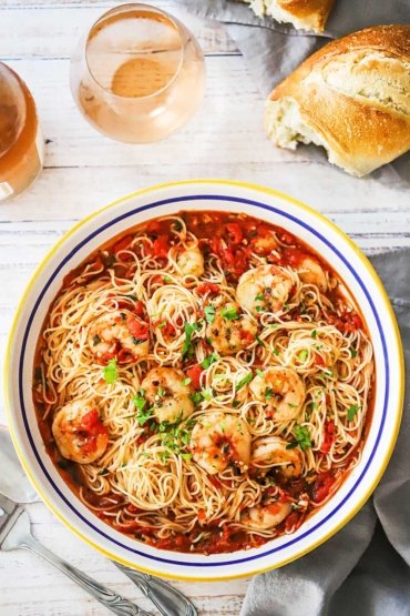 An overhead view of a large pasta bowl filled with shrimp marinara sitting next to a couple glasses of rosé wine.