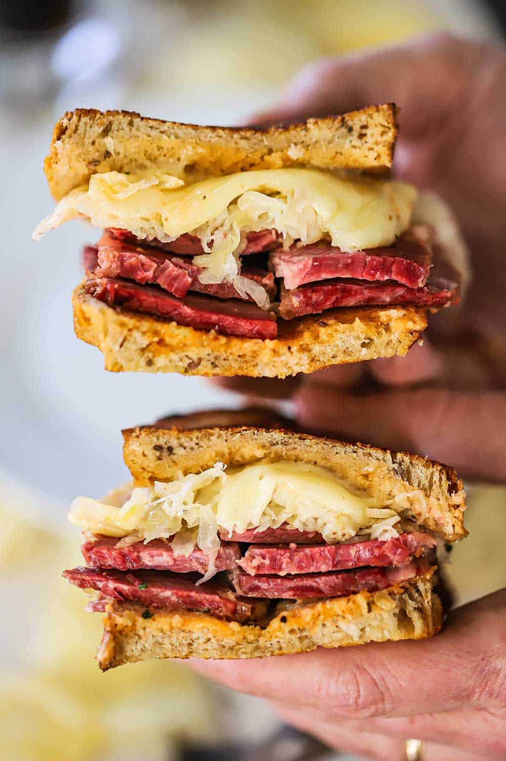 Two hands holding two halves of a grilled rueben sandwich exposing the thick cut corned beef, sauerkraut, and and melty Swiss cheese.