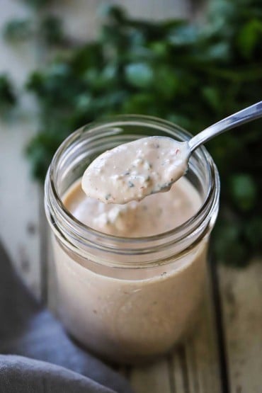A small glass jar filled with Russian dressing with a spoon lifting some of it out of the jar.