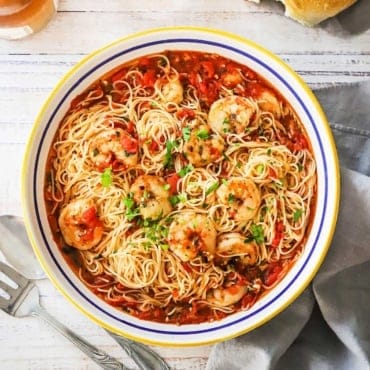 An overhead view of a large pasta bowl filled with shrimp marinara sitting next to a couple glasses of rosé wine.