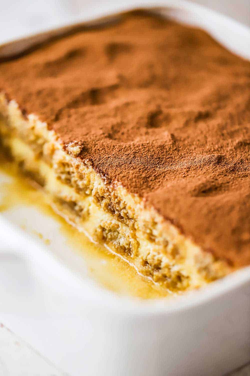 A square white baking dish filled with tiramisu with half of it removed.