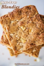 An overhead view of a stack of blondies that are studded with walnuts, white chocolate morsels, and toffee.