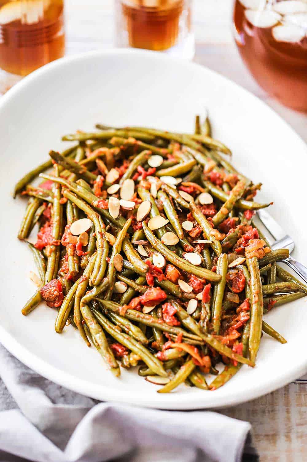 A large white serving dish filled with braised green beans with tomatoes and topped with almond slices.